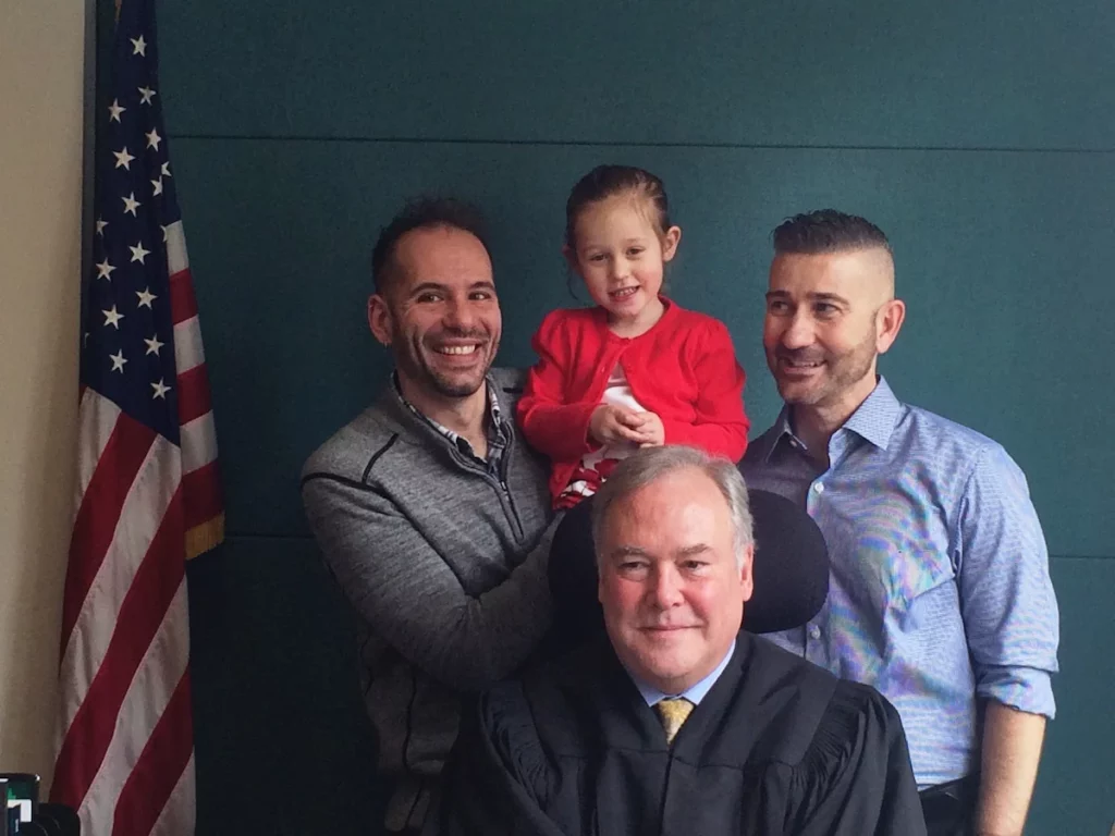 Two dads with their daughter posing with a judge on adoption day