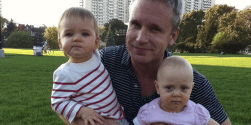 Dad sitting in the park holding his twin infant daughters