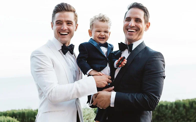 Greg Berlanti & Robbie Rogers with their son all dressed in tuxedos