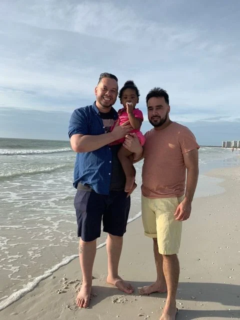 two dads with their daughter on the beach