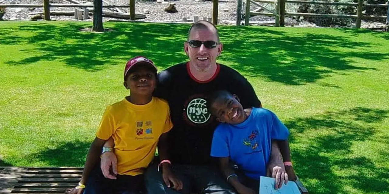White gay father sitting on a park bench with his two African American sons.