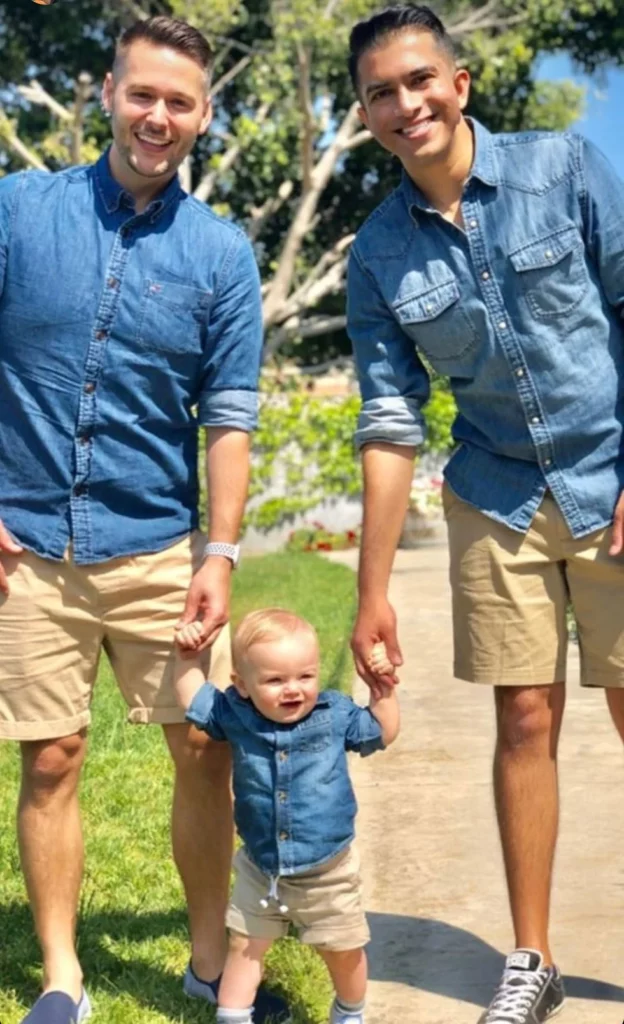 Two dads and their toddler posing in matching tan shorts and denim shirts