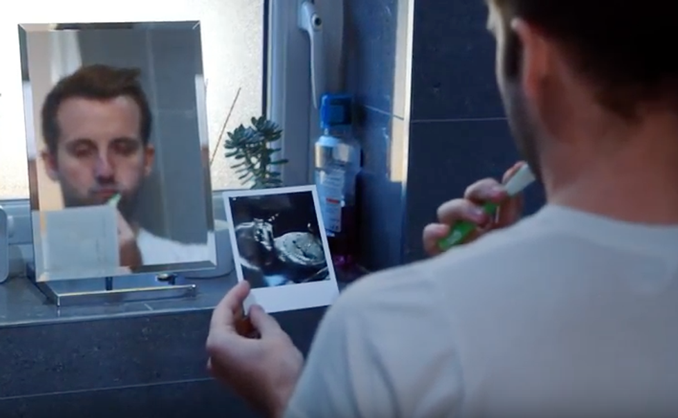 Man in bathroom brushing his teeth and looking at sonogram picture