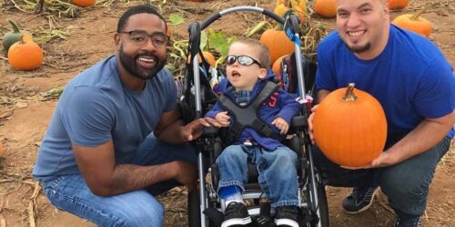 Two fathers with their son in a pumpkin patch