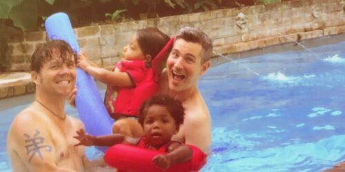 two dads and their daughters playing in a pool
