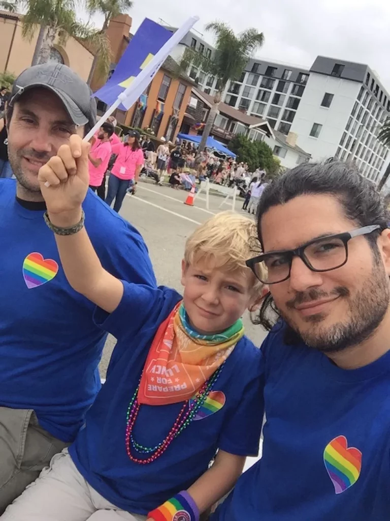 Two dads with their son in matching shirts walking in the Pride Parade
