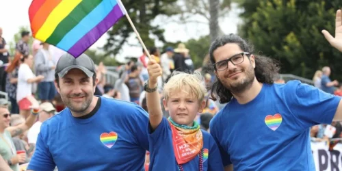 Two dads with their son holding a Pride Flag at Pride