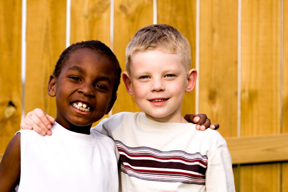 two little boys one black one whitw with arms on each others shoulders