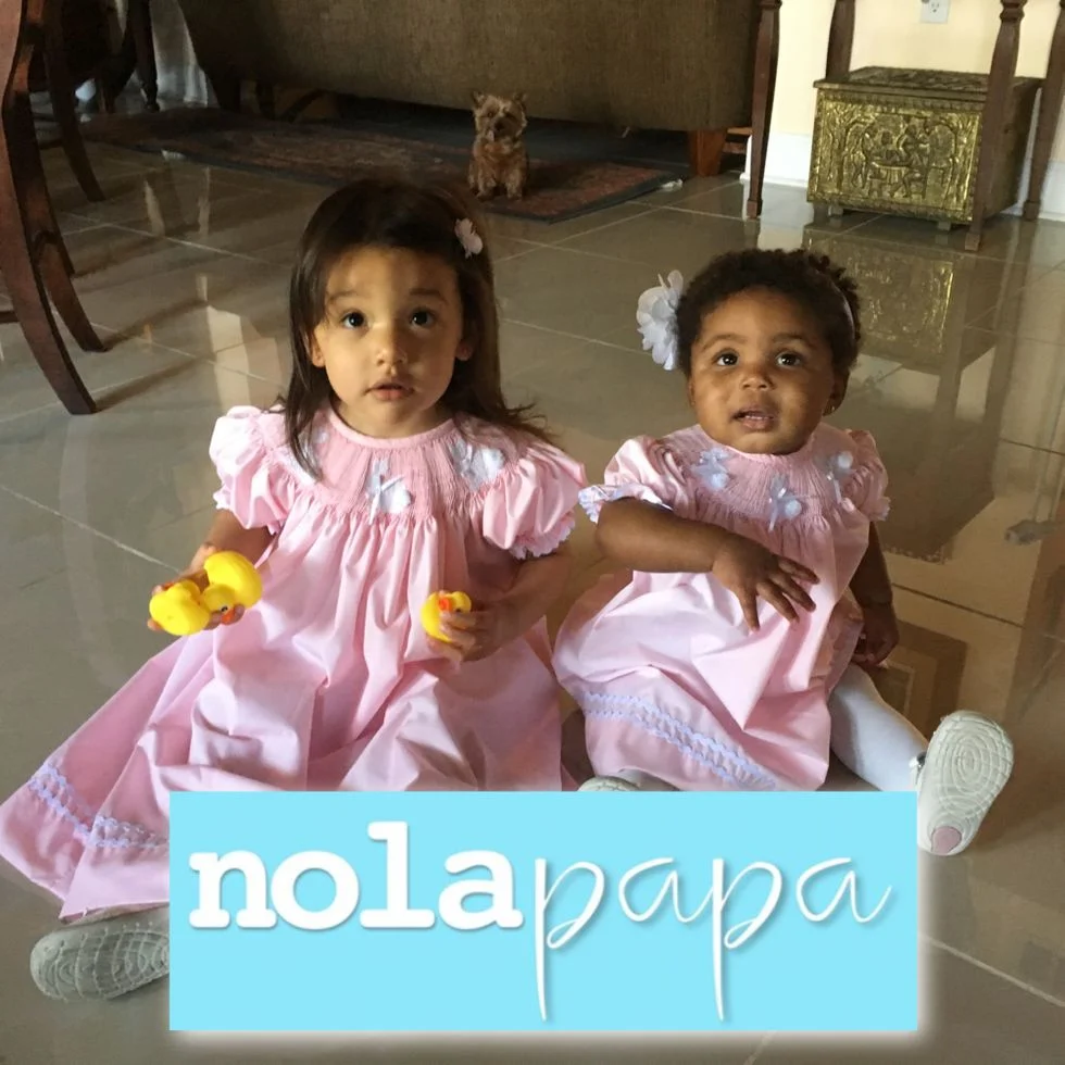 Two little girls sitting on the floor in pink dresses holidng rubber duckies