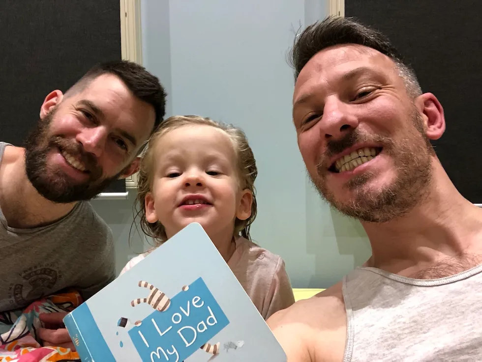 Little girl reading a book with her two dads
