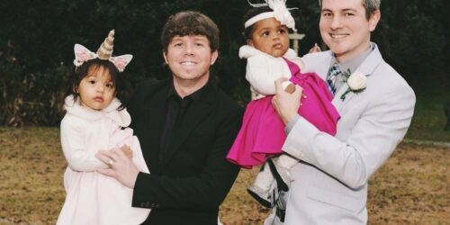 Two dads in suit holding their toddler daughters all dressed up