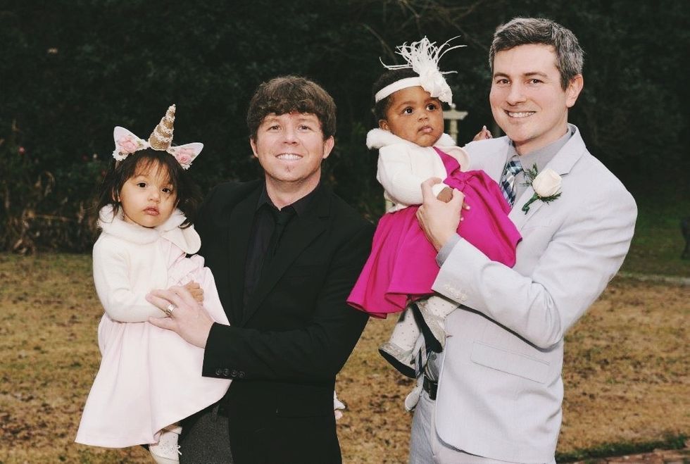 Two dads in suit holding their toddler daughters all dressed up