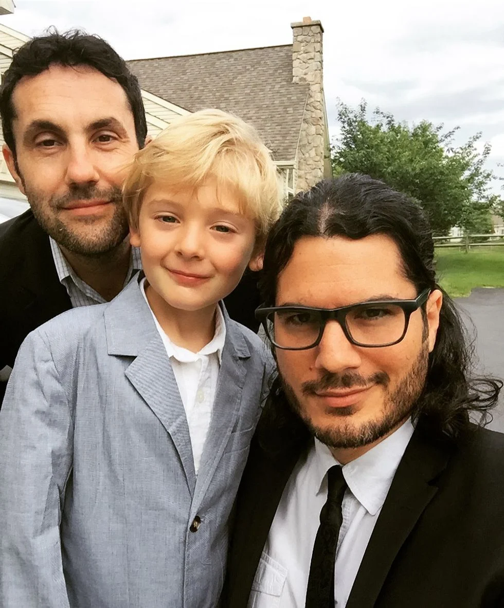 Two dads with their son dressed in suits on the front lawn