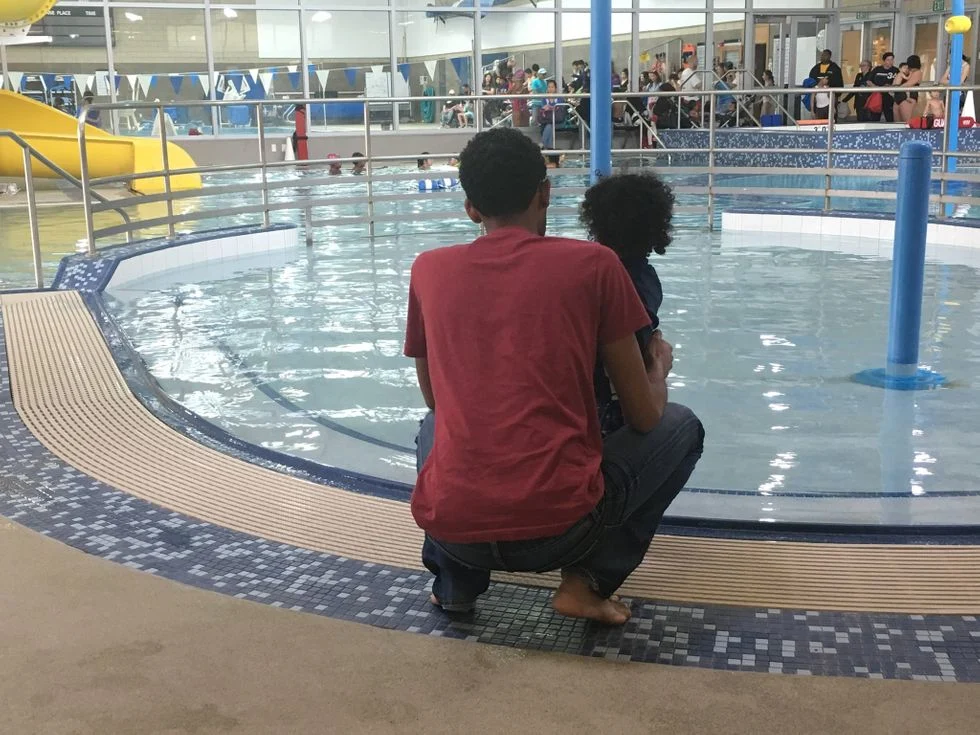 The backs of a man and child on the edge of an indoor pool
