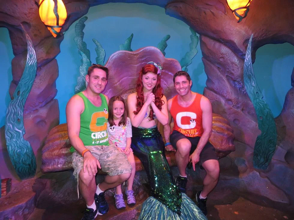 Two men and a little girl sitting with Ariel at Disney