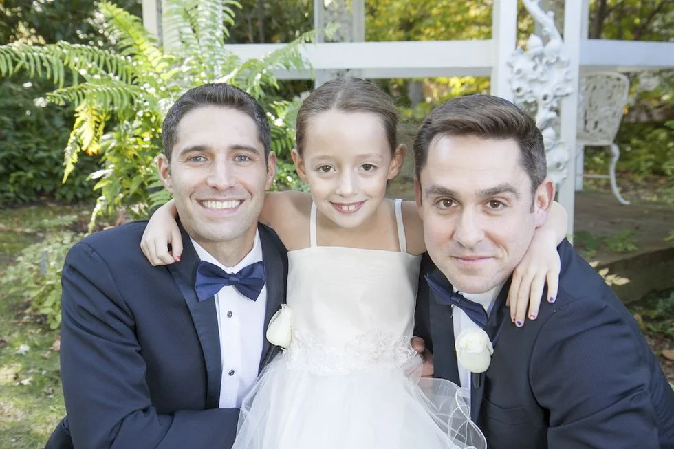 Two men in tuxedos and a little girl in white flower girl dress