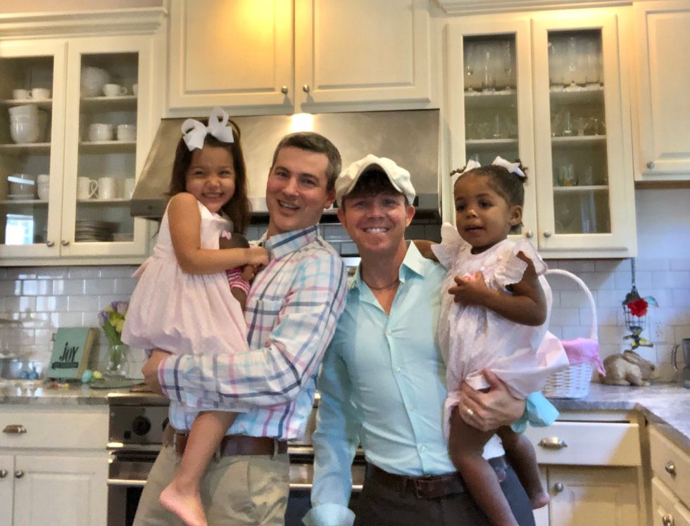 Two dads holding their daughters in their kitchen