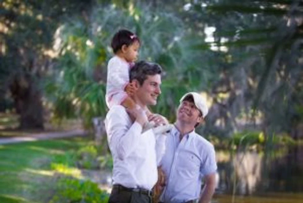 Two dads walking in park with their daughter on one of her dad's shoulders