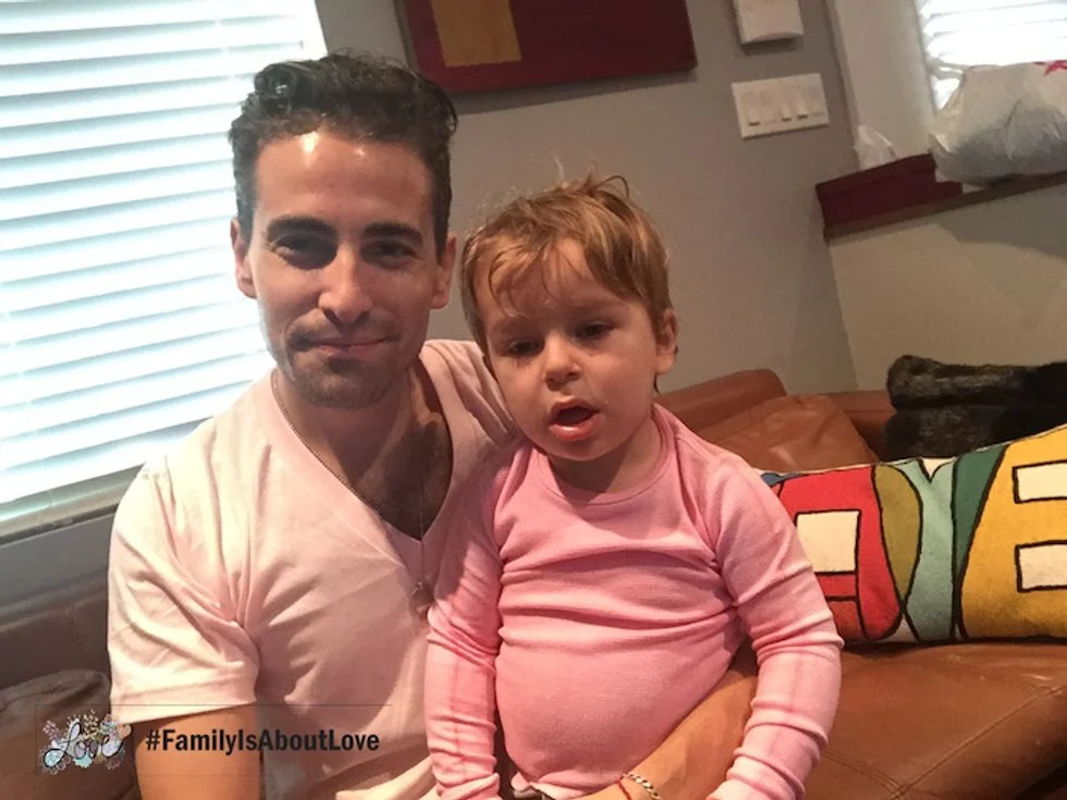 Toddler boy sitting on the couch with his dad wearing a pink shirt
