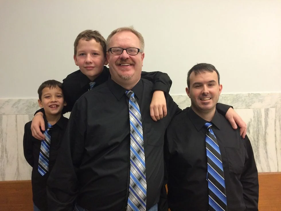 Two dads with their foster sons in matching black shirts and ties