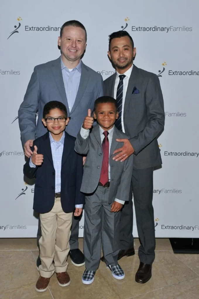 Two foster dads with their sons dressed up in suits giving the thumbs up