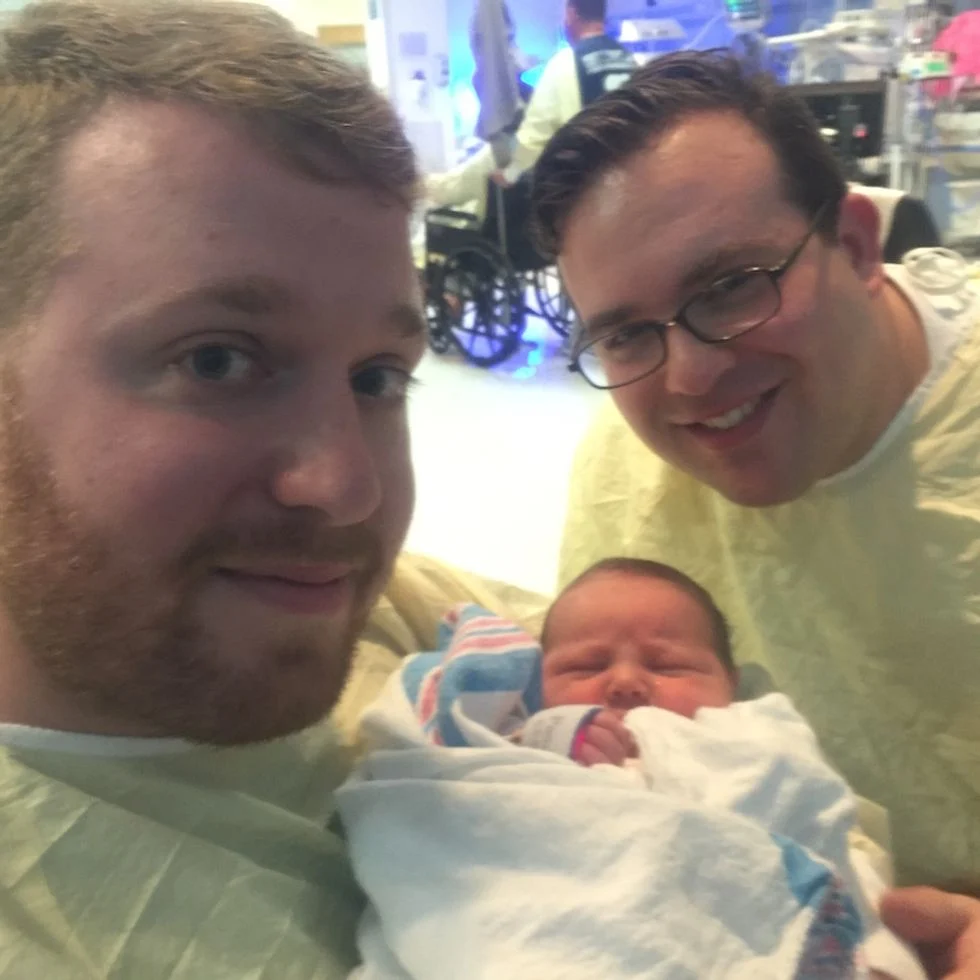 two dads in scrubs holding their newborn son