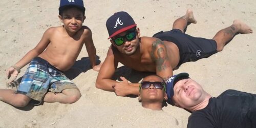 Two dads with their two sons on the beach one buried in the sand