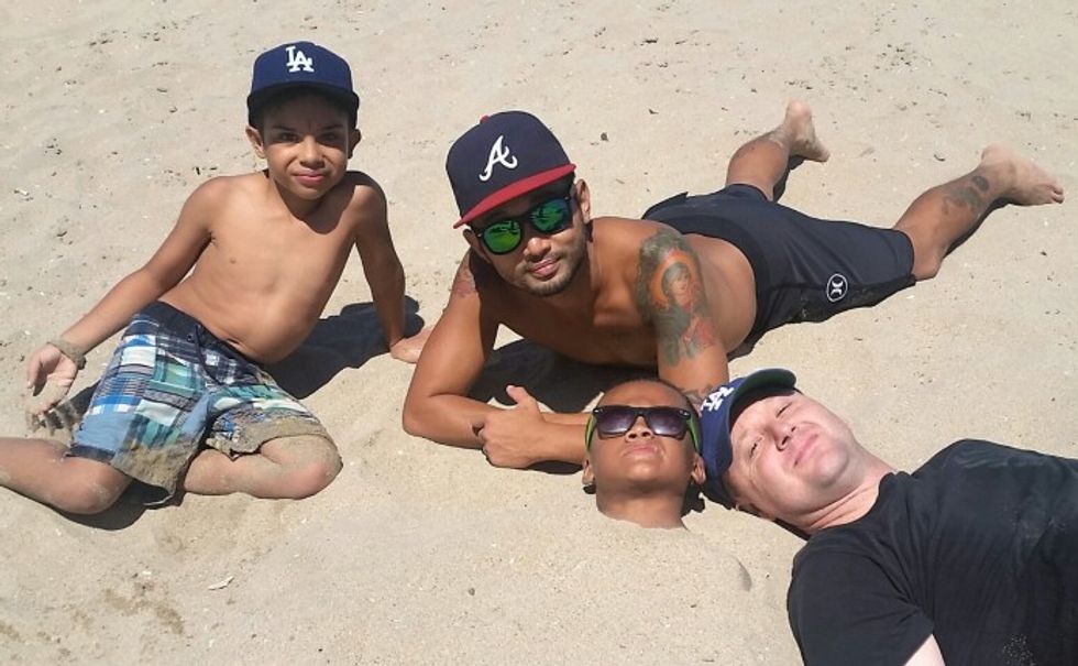 Two dads with their two sons on the beach one buried in the sand