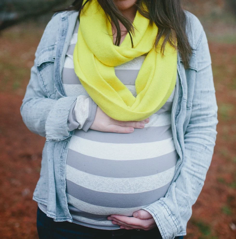pregnant woman wearing a yellow scarf craddling her pregnant belly