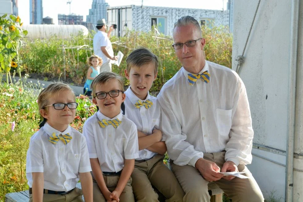 Dad posing with his three sons on a rooftop garden wearing matching bow ties