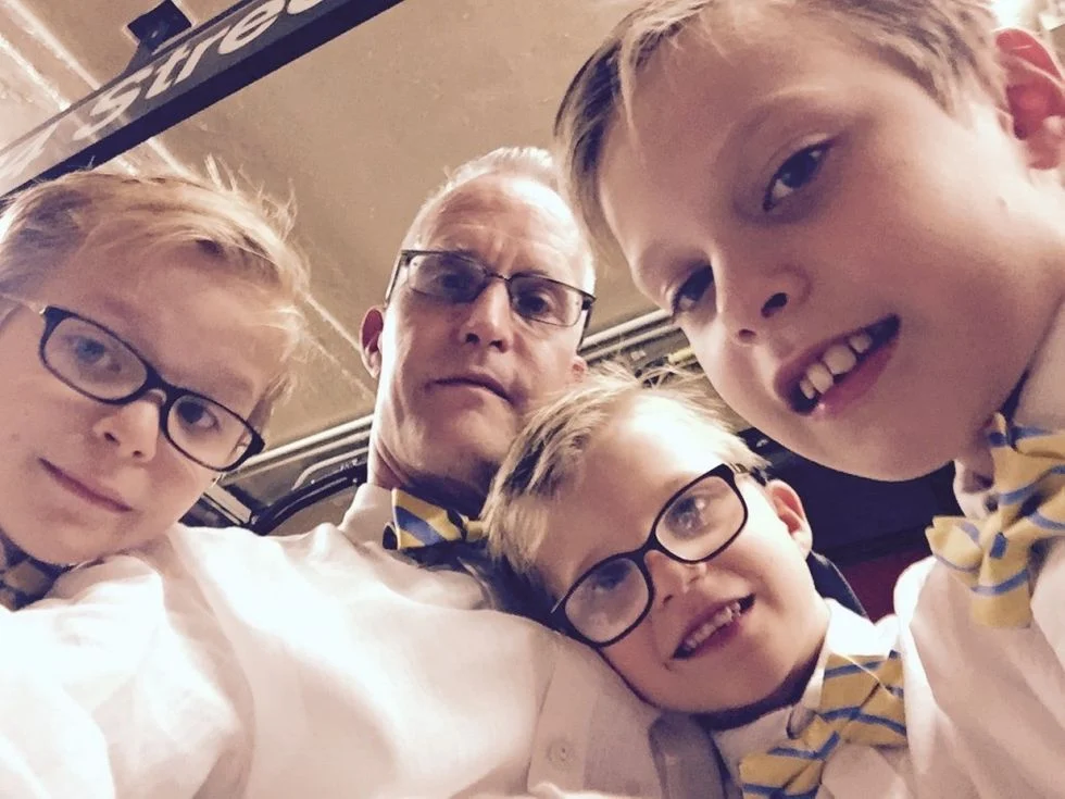 Dad taking a selfie with his three sons wearing matching bow ties
