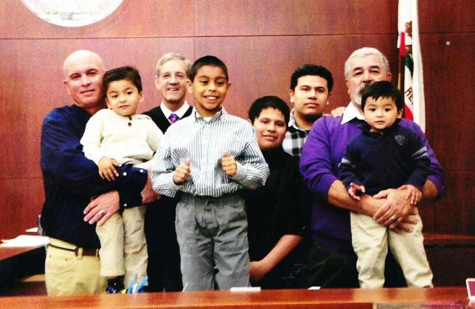 Two dads with their five children in a courtroom with a judge on adoption day.