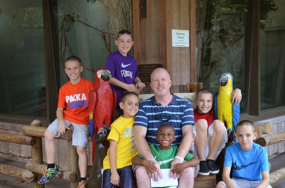 Dad posing with his six boys at a zoo exhibit