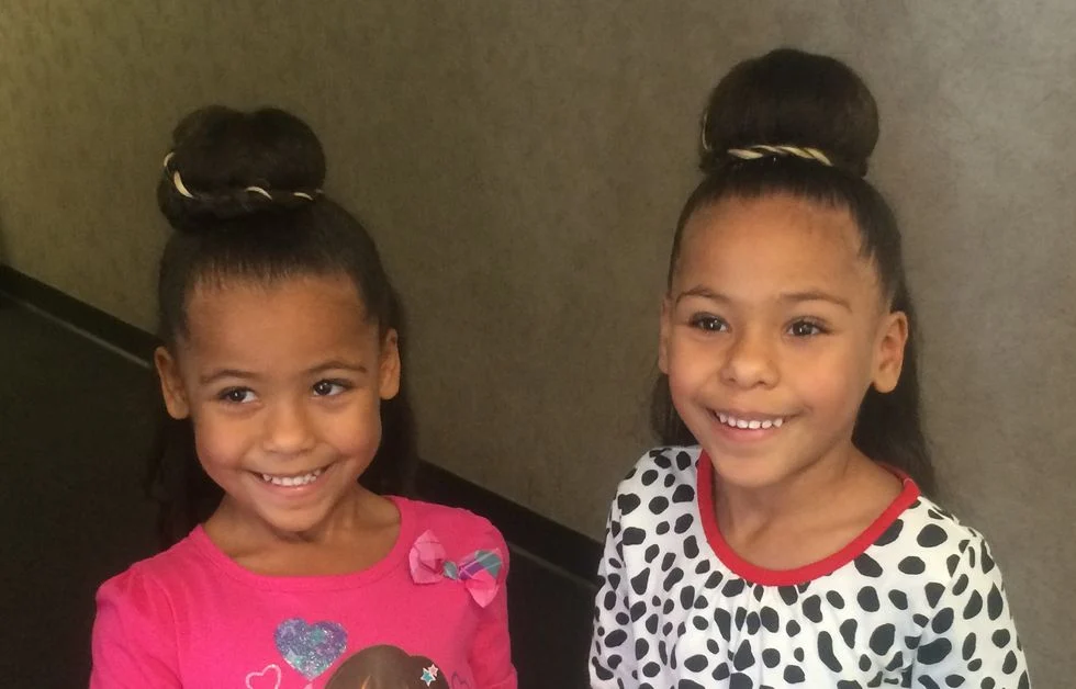 Two little girls smiling wearing matching buns