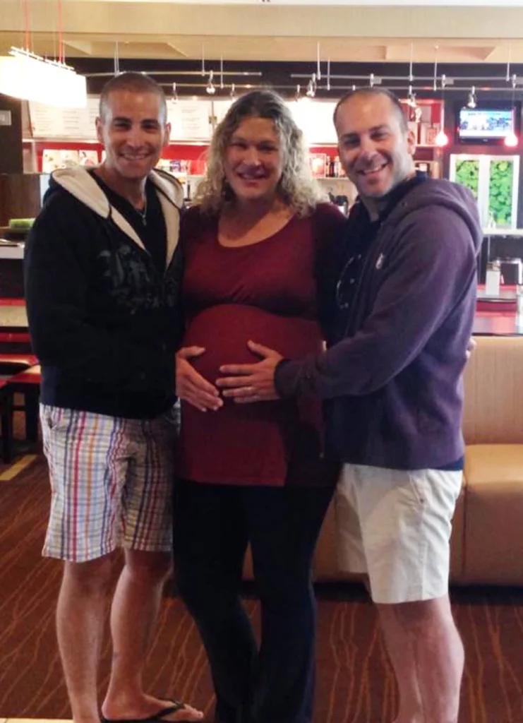 Two dads standing with their surrogate - holding her belly