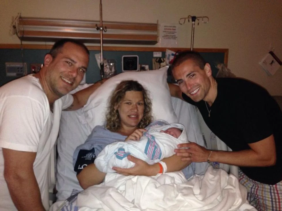 Two dads in hospital with their surrogate and newborn baby