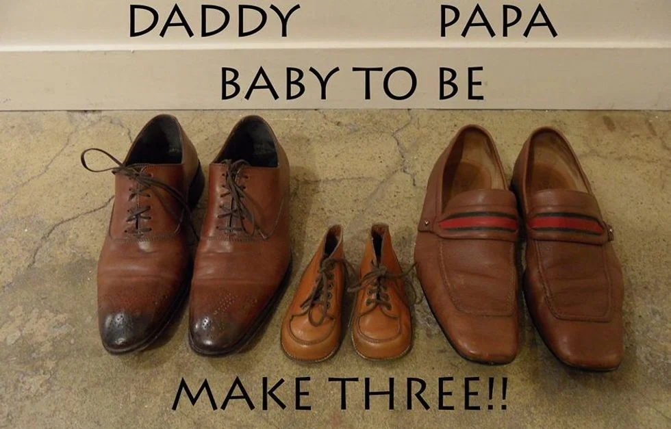 Pregnancy announcement photo featuring two pairs of men's dress shoes and a pair of baby shoes