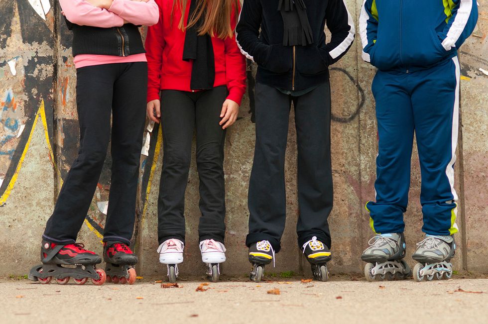 four children leaning against wall with roller skates on