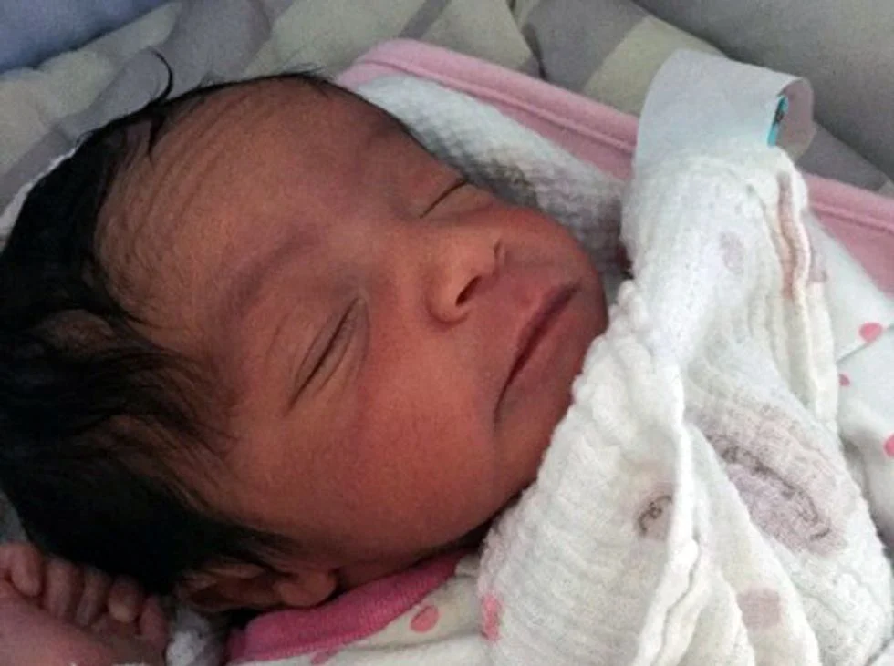 Newborn baby girl with dark hair in blanket