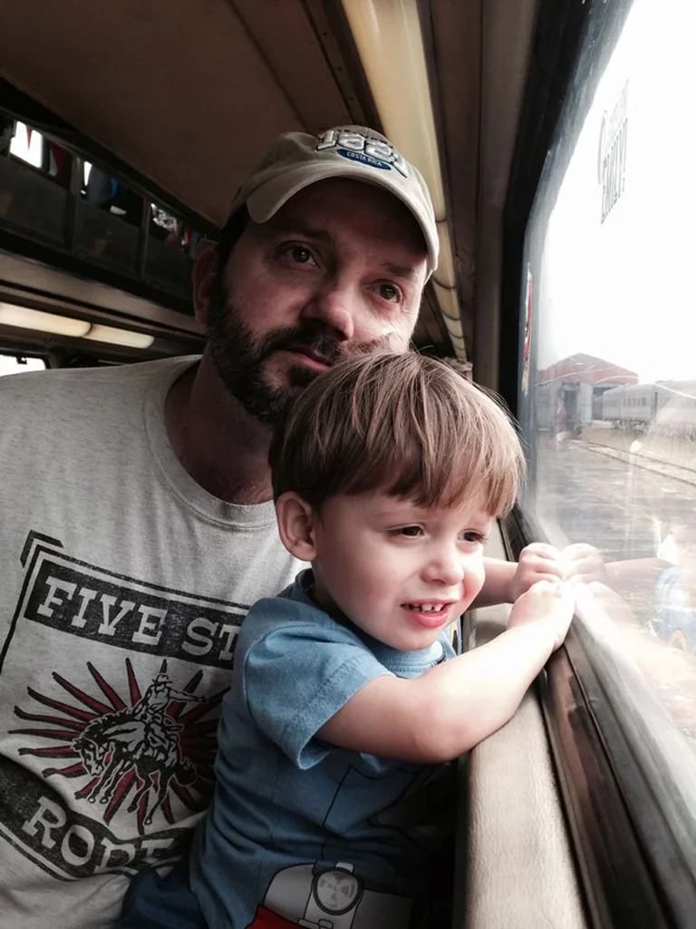 Father and toddler son sitting on a train looking out the window