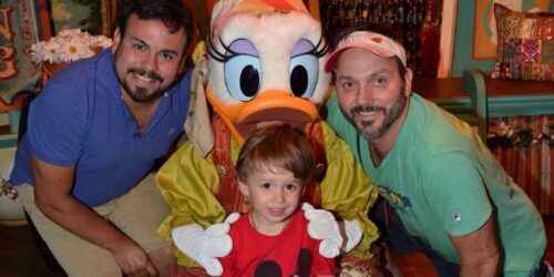 Two dads and their son posing with Daisy Duck