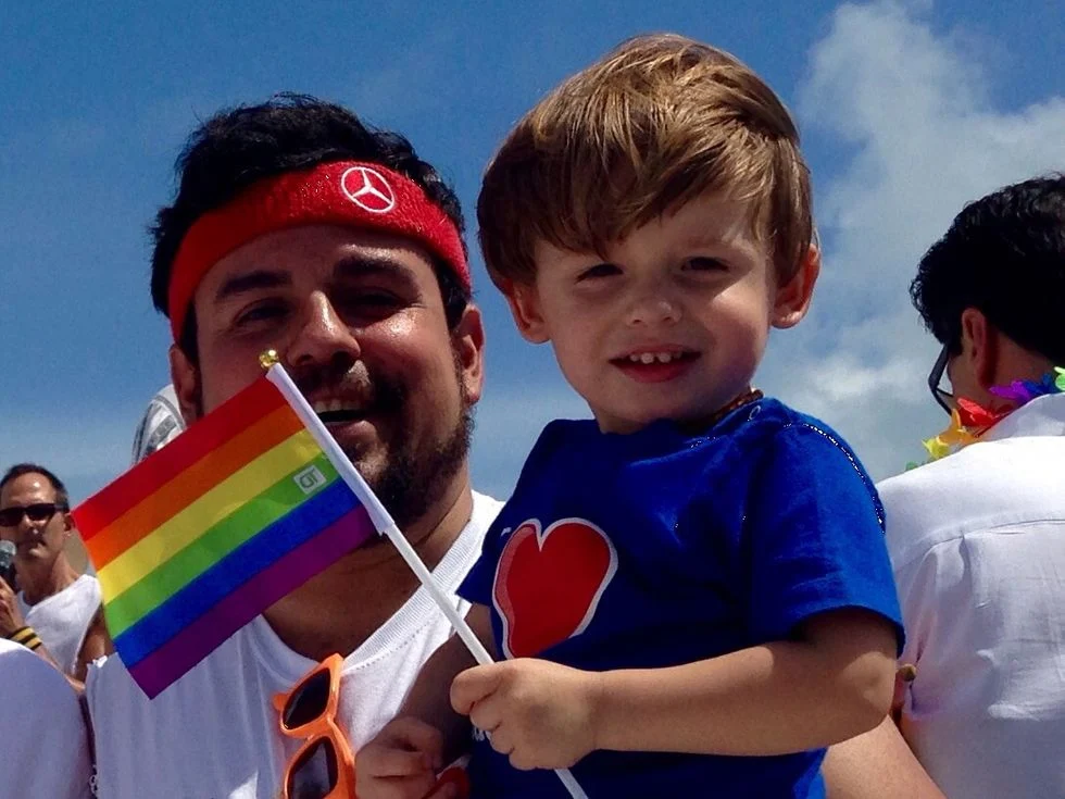 Father holding his son at Pride Parade.  Toddler is holding the gay pride flag