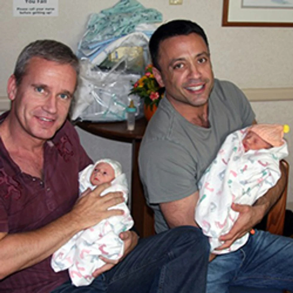Two fathers each holding one of their newborn twins