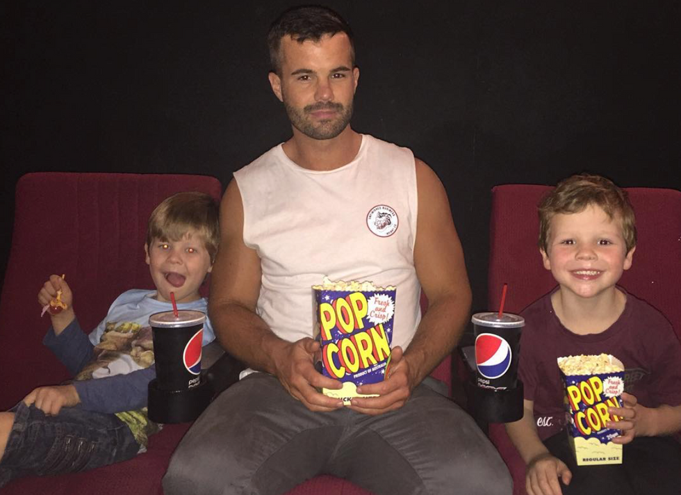 Man sitting between two boys at a movie theatre all holding popcorn