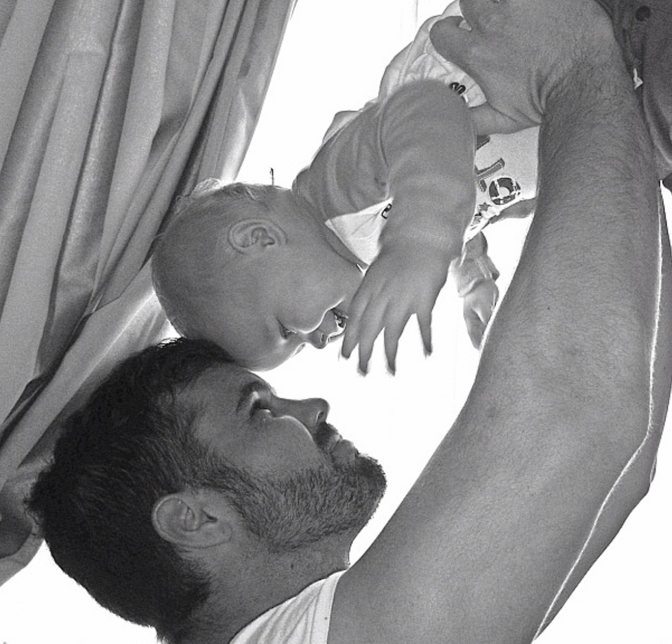 A profile black and white photo of a man holding a baby up in the air
