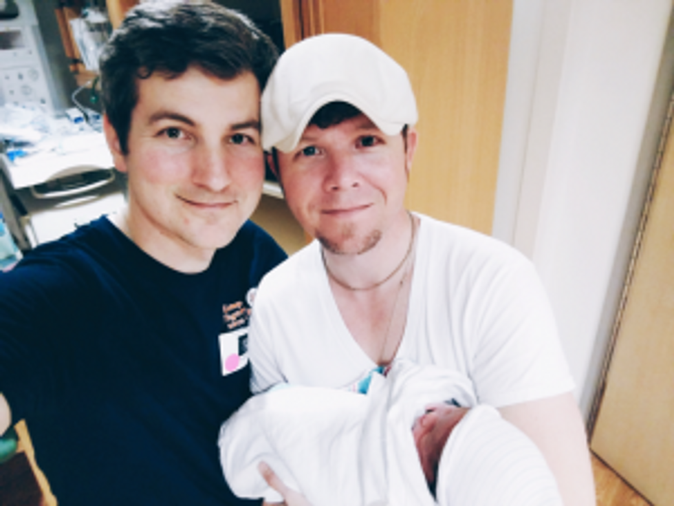 Two dads holding their newborn daughter in the hospital