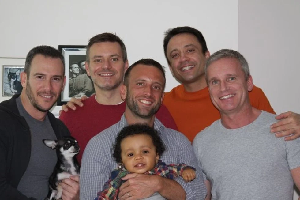 Five men standing.  One holding a small dog the other a small child