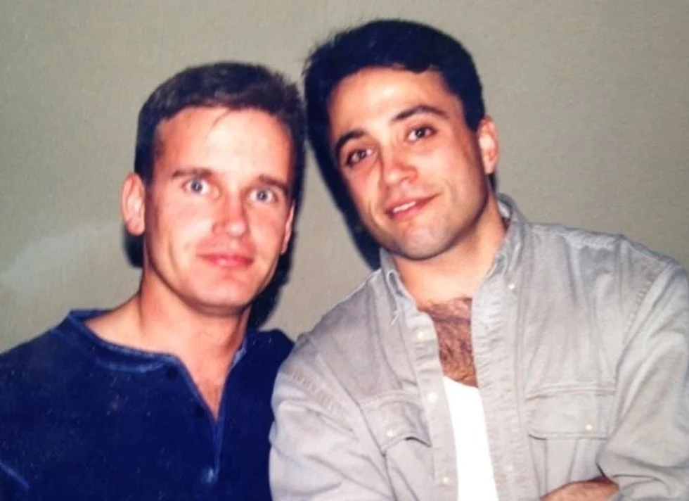 Two men posing tother one in a gray shirt and one in a blue shirt