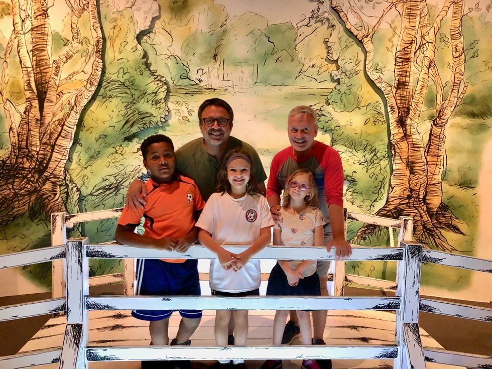 Family of five - two dads, two daughers and one son posing on a Winnie The Pooh bridge