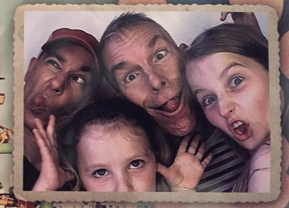 two dads posing with their daughters in a picture frame making funny faces